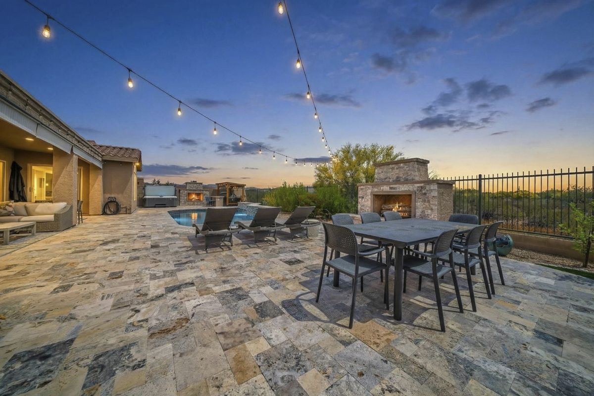 Travertine patio with outdoor fireplace and string lights at dusk, Anthem