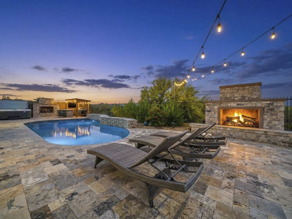 Travertine patio with loungers and fireplace at dusk, Anthem