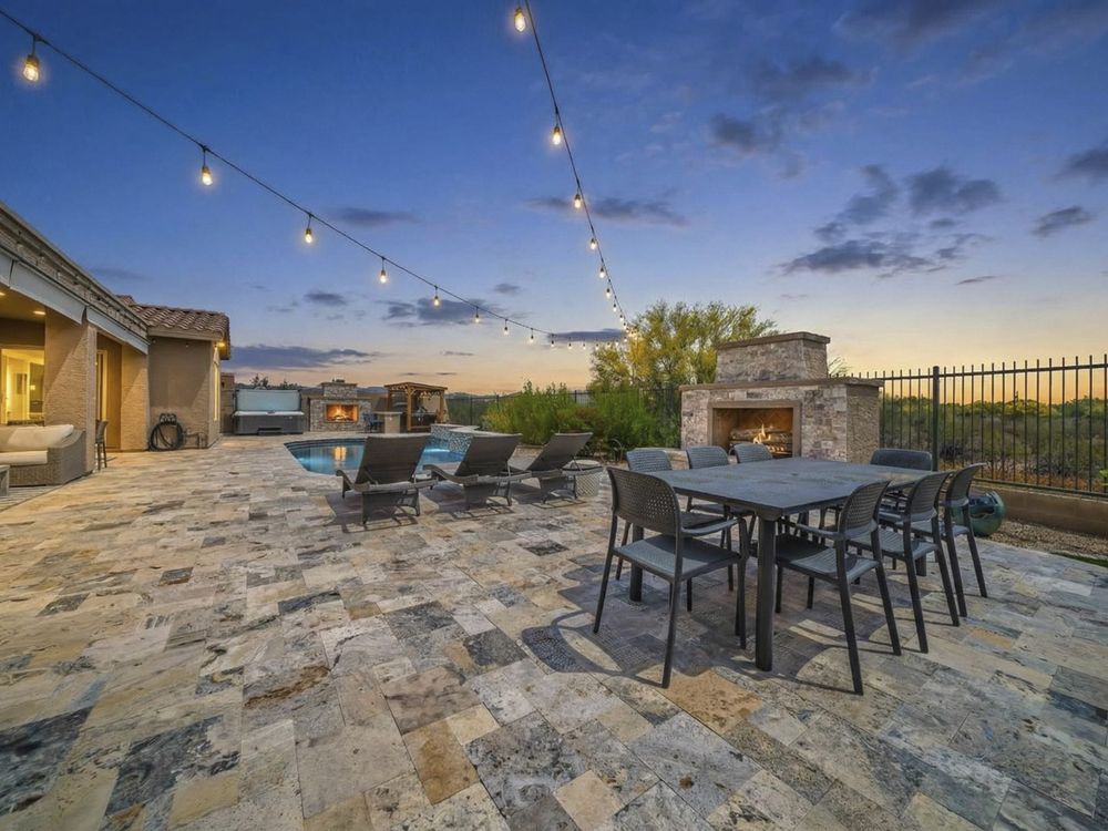 Travertine patio with dining table, fireplace and string lights, Anthem